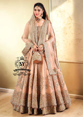 In a radiant shade of Peach puff, this bridal dress captures a timeless grandeur, sweetened with touches of pastel romance. This open-cut kalidaar gown shines with tissue silk lehenga.