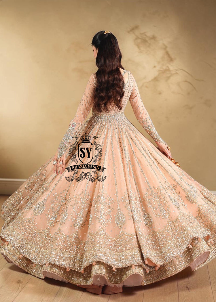 In a radiant shade of Peach puff, this bridal dress captures a timeless grandeur, sweetened with touches of pastel romance. This open-cut kalidaar gown shines with tissue silk lehenga.