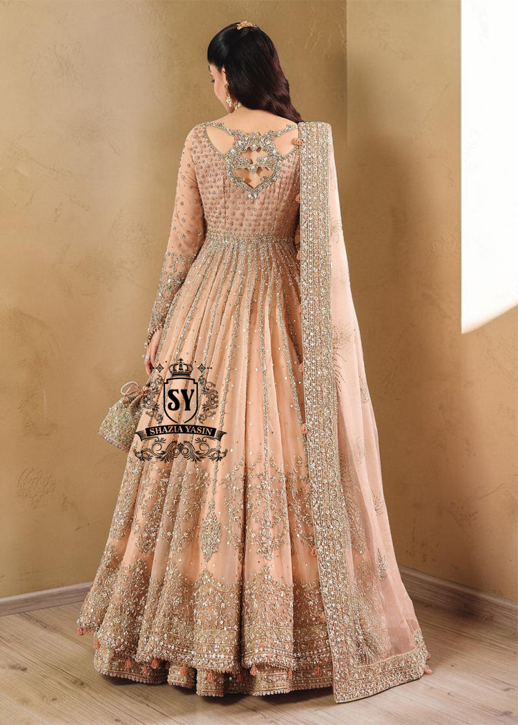 In a radiant shade of Peach puff, this bridal dress captures a timeless grandeur, sweetened with touches of pastel romance. This open-cut kalidaar gown shines with tissue silk lehenga.