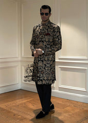 This luxurious royal black velvet sherwani, adorned with opulent gold hand embroidery, exudes a bold and dignified presence. The plush velvet fabric highlights the depth of the intricate hand embellishments, creating a truly regal style befitting a groom or a grand ceremony.