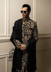 This luxurious royal black velvet sherwani, adorned with opulent gold hand embroidery, exudes a bold and dignified presence. The plush velvet fabric highlights the depth of the intricate hand embellishments, creating a truly regal style befitting a groom or a grand ceremony.