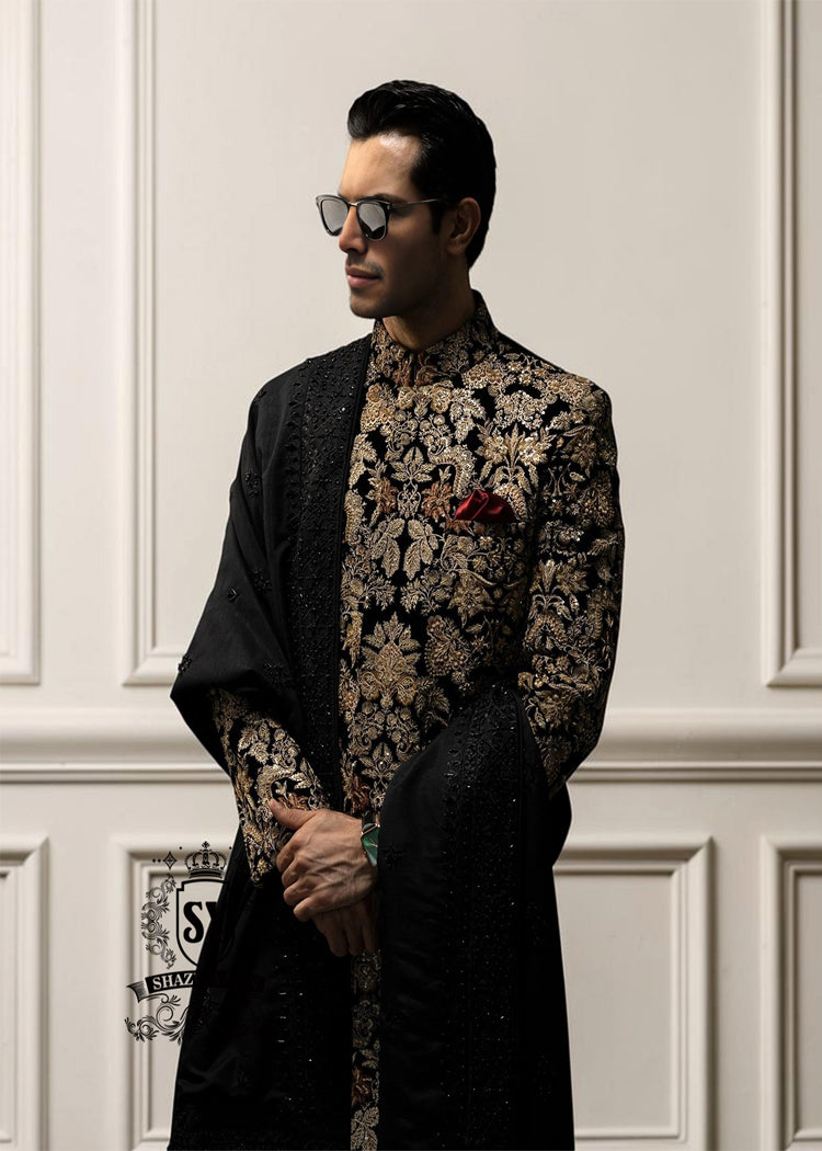 This luxurious royal black velvet sherwani, adorned with opulent gold hand embroidery, exudes a bold and dignified presence. The plush velvet fabric highlights the depth of the intricate hand embellishments, creating a truly regal style befitting a groom or a grand ceremony.