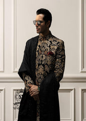 This luxurious royal black velvet sherwani, adorned with opulent gold hand embroidery, exudes a bold and dignified presence. The plush velvet fabric highlights the depth of the intricate hand embellishments, creating a truly regal style befitting a groom or a grand ceremony.